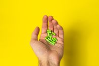 From above of crop unrecognizable male demonstrating green pills in hand against yellow background in daylight