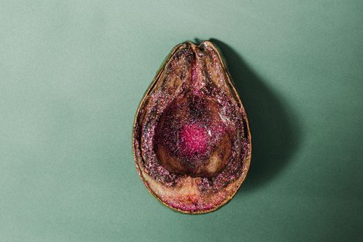 From above of half of rotten avocado covered with pink glitter placed on green background in studio