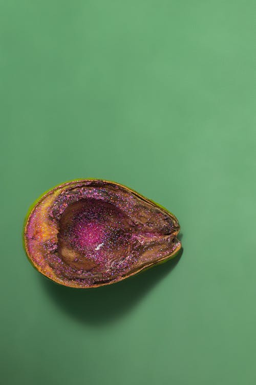 Isolated half of avocado with pink glitter placed on green surface in studio