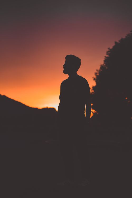 Free A silhouette of a man against a warm, vibrant sunset with hills in the background creating a captivating scene. Stock Photo