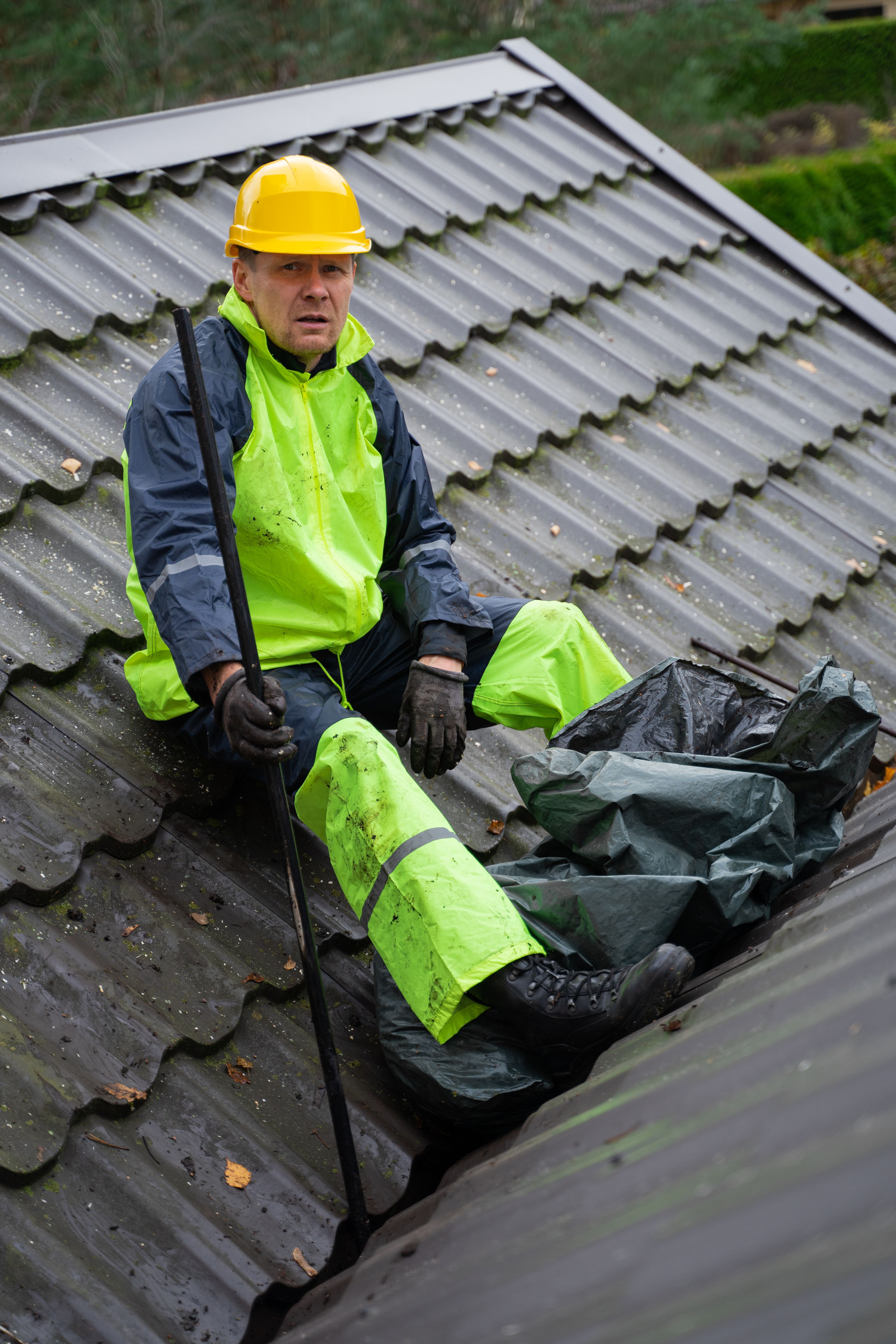 Roofer in high-visibility gear clearing debris from a tiled valley