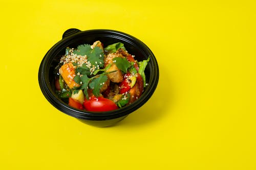 From above of delicious healthy salad consisting of various vegetables in plastic bowl placed on bright yellow background