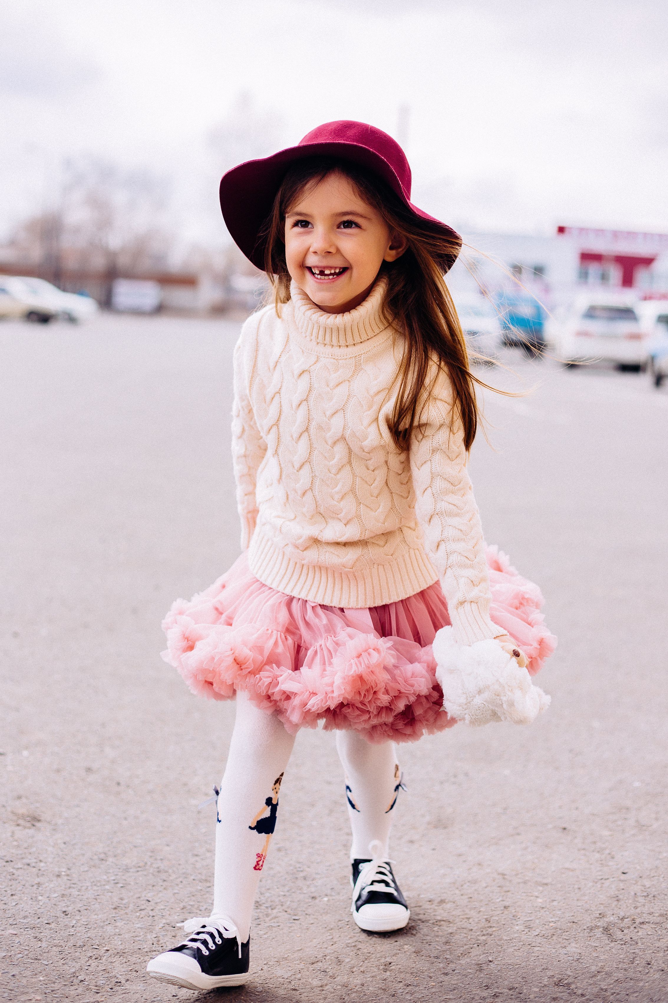 Garota sorridente em um suéter de malha fashion e tutu aproveitando um dia fora.
