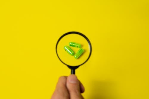 Crop person holding magnifier above pills