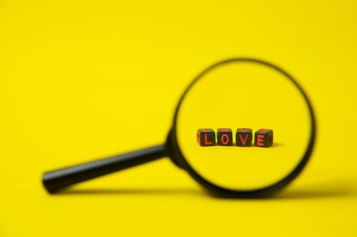 Free Love sign made of black plastic cubes with letters placed near magnifying glass on bright yellow background Stock Photo