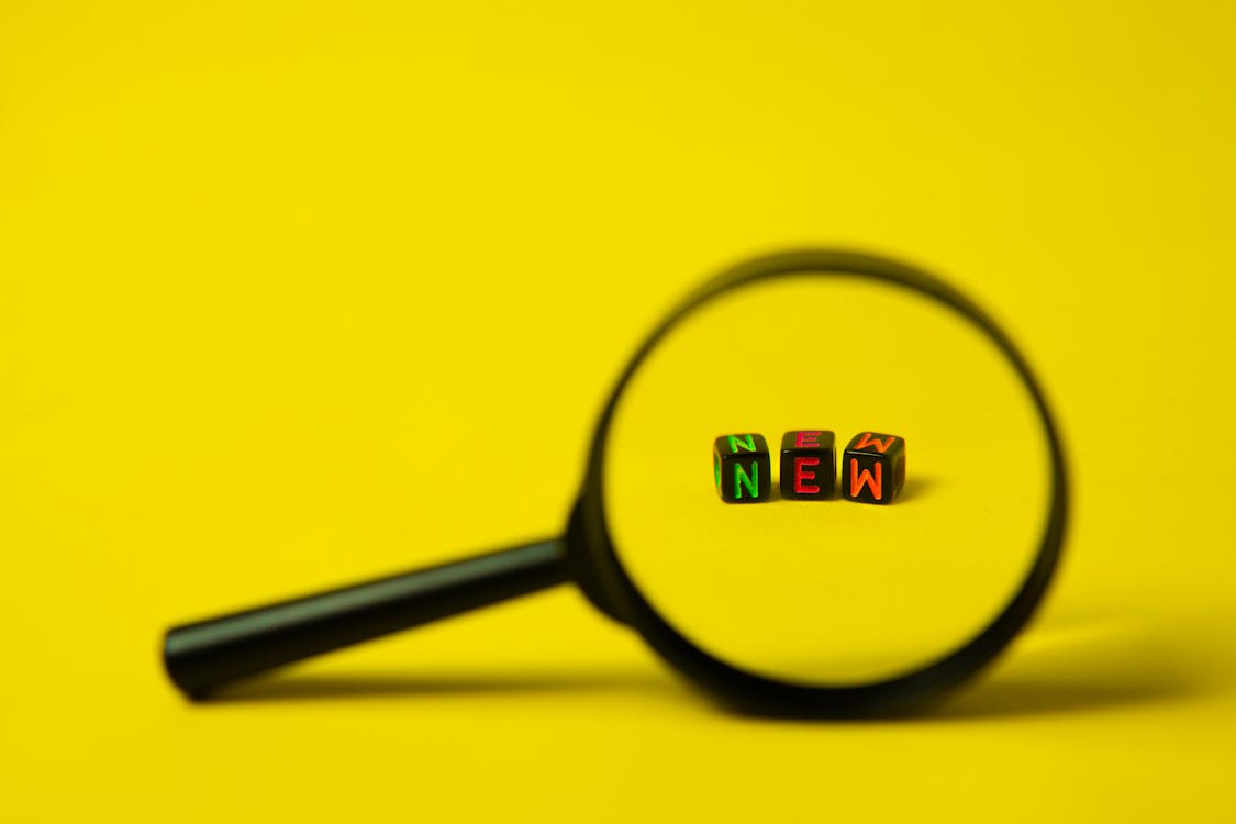 Free Concept image of big black magnifier with word new in form of cubes against yellow background Stock Photo