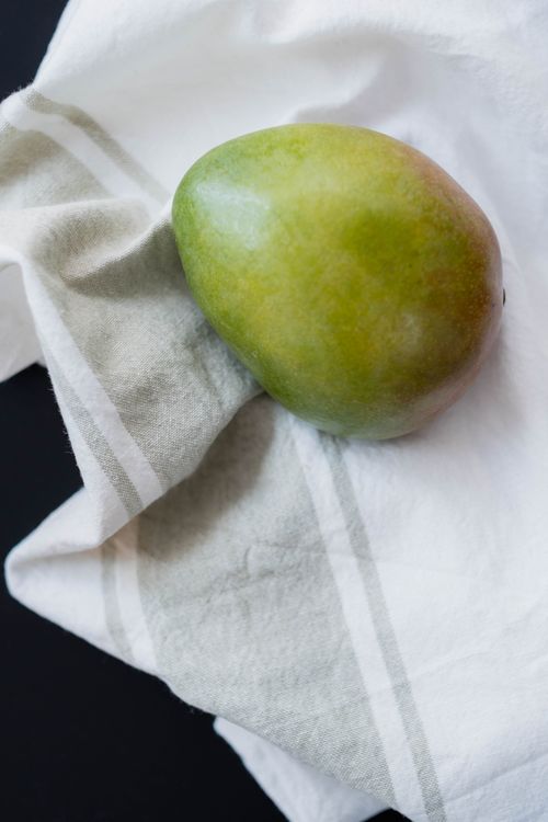 Free Close-up of a fresh mango resting on a textured linen cloth, perfect for food or kitchen themes. Stock Photo