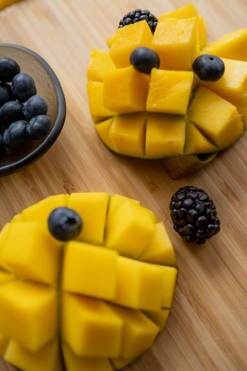 Free Sliced mangos and assorted berries on wooden background, perfect for healthy eating concepts. Stock Photo