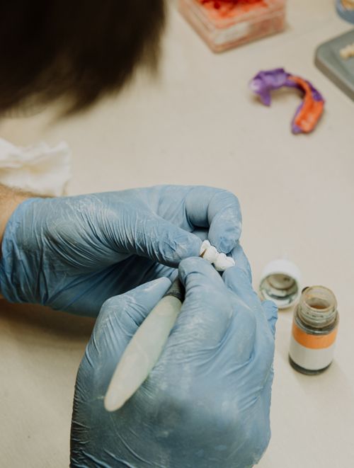 Free Crop anonymous orthodontist in latex gloves creating fake teeth using dental tools while sitting at table in dental clinic Stock Photo