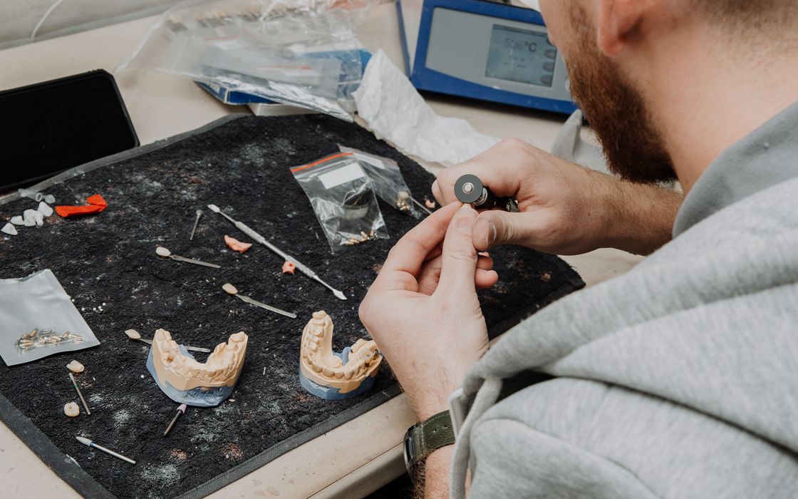 Dental technician working on a denture at a lab bench with plaster models and instruments