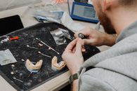 From above of crop anonymous male master sitting at table during creating denture and working with dental impression in modern dental clinic