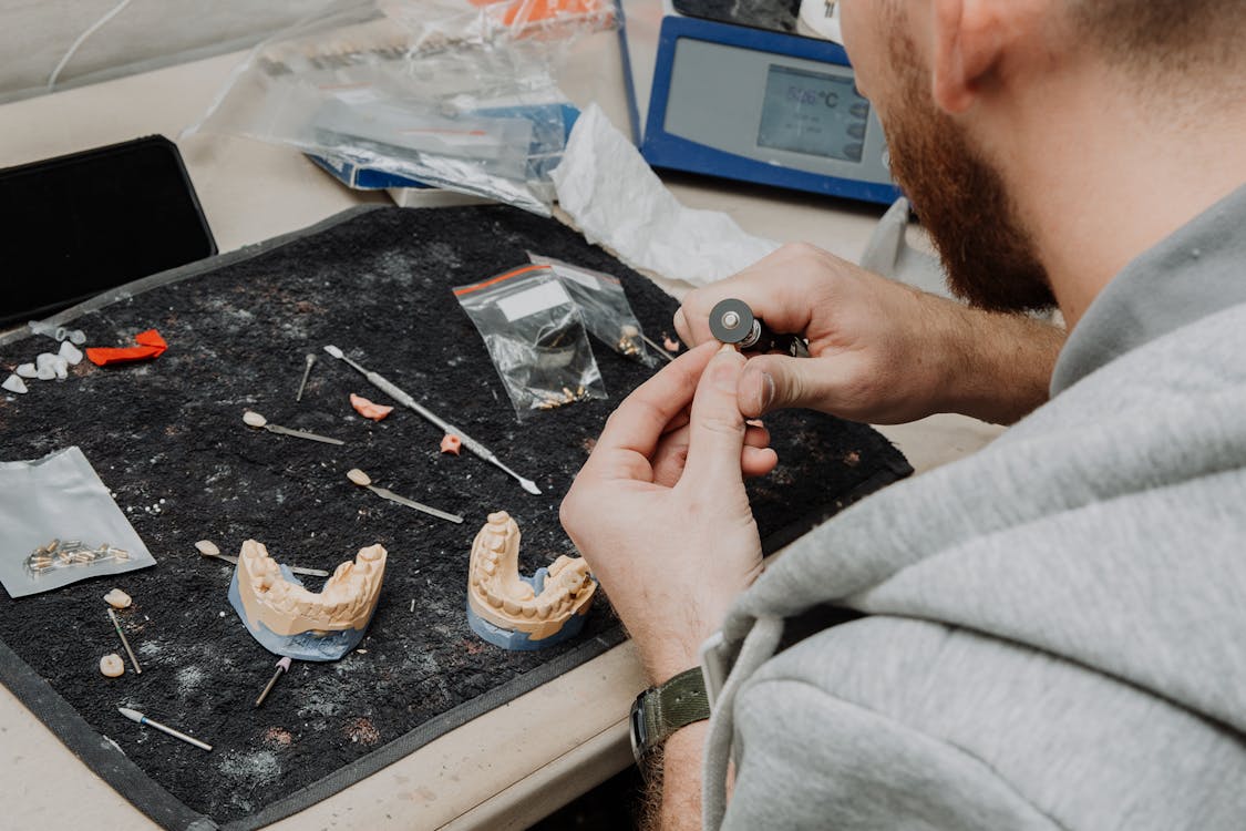 Free From above of crop anonymous male master sitting at table during creating denture and working with dental impression in modern dental clinic Stock Photo