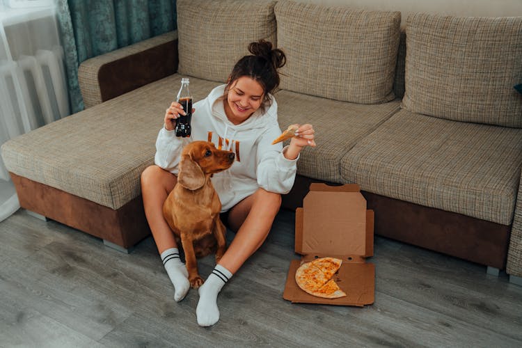 Happy Woman Sitting With Dog And Eating Pizza