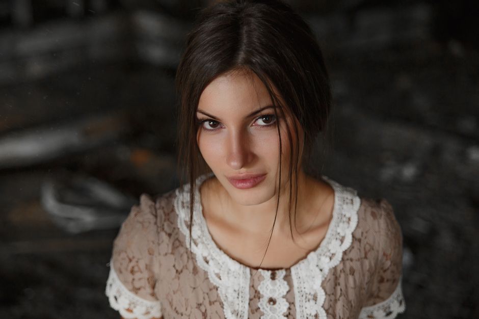 Close-up portrait of a young woman in a lace blouse with brown hair and captivating gaze.