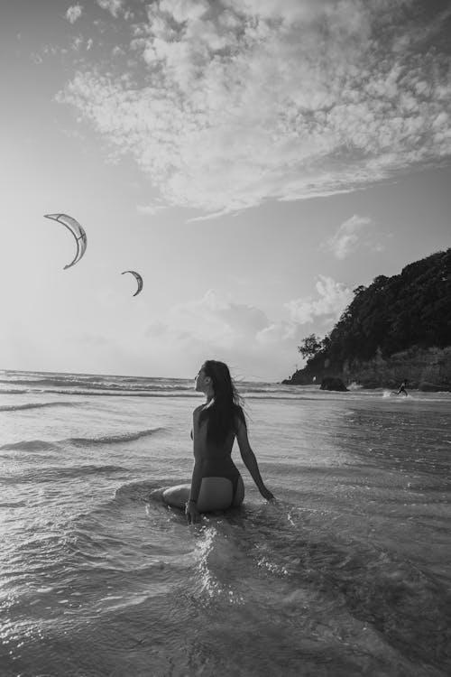 Woman Sitting on Sea Shore near Flying Kites