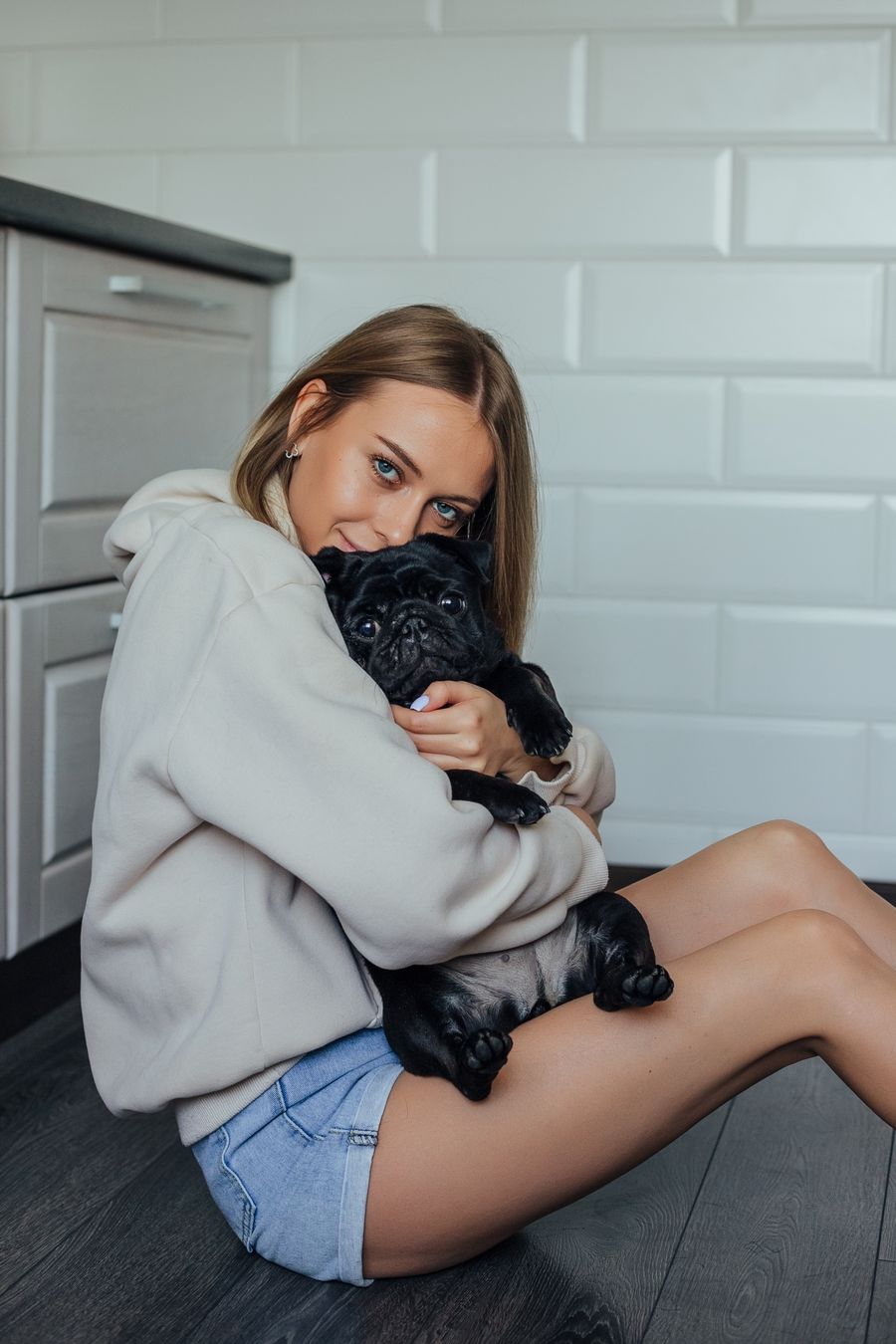 An indoor portrait of a woman hugging her black pug