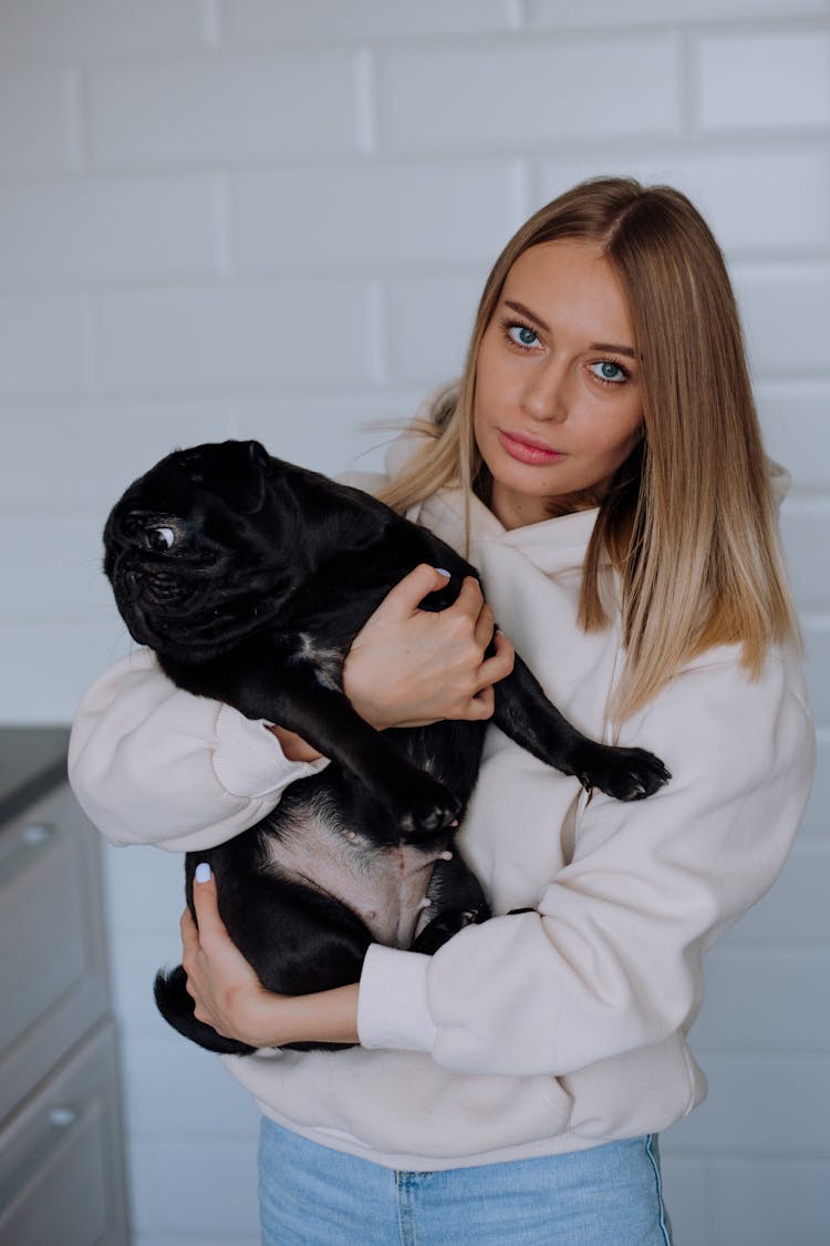 
A Woman In A Hoodie Holding A Pug