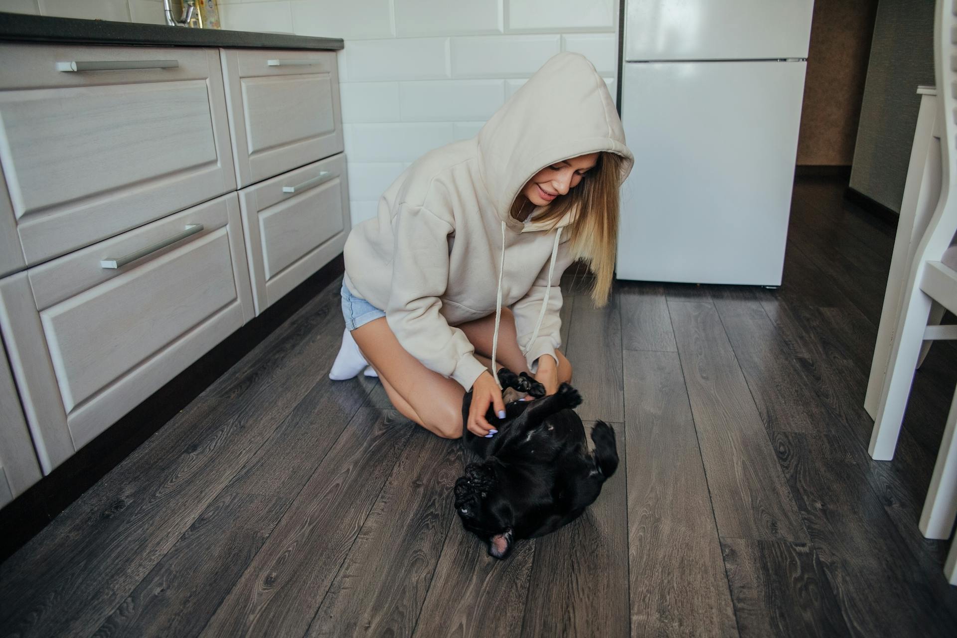 A Woman in a Hoodie Tickling Her Pet Pug