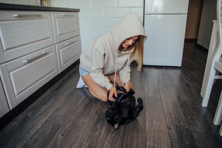 
A Woman In A Hoodie Tickling Her Pet Pug