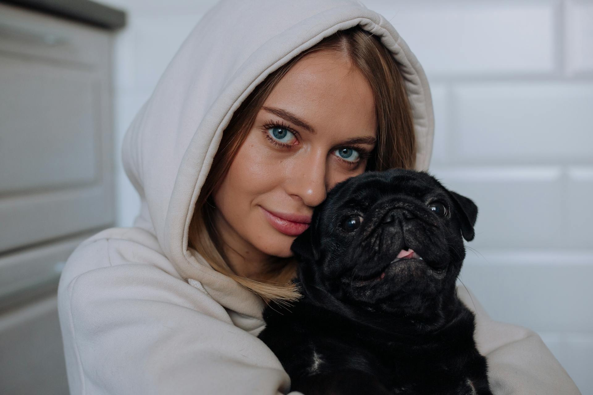 A Woman in a Hoodie Hugging Her Pet Pug