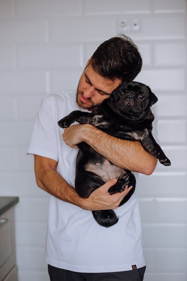 
A Man In A White Shirt Hugging His Pet Pug