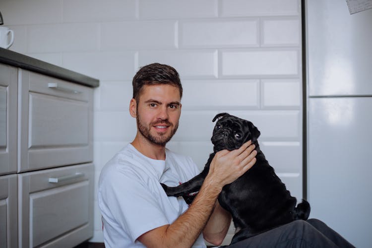 

A Man In A White Shirt With His Pet Pug