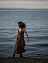 穿着飘逸衣服的女人在日落时分沿着海边散步，捕捉到一个宁静的时刻