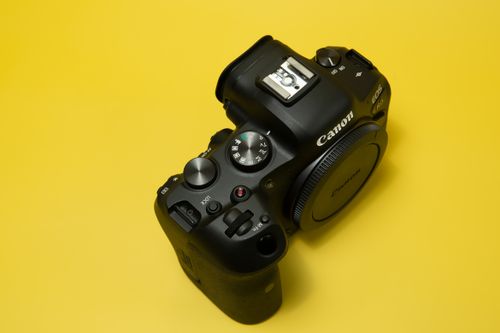 Free Close-up of a professional DSLR camera against a vibrant yellow background, showcasing detailed controls. Stock Photo