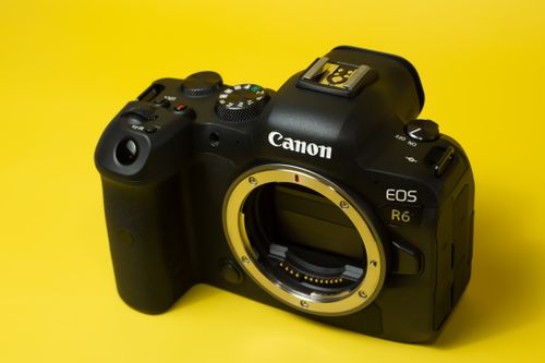 Free Close-up of a black mirrorless camera on a vibrant yellow background for tech and photography themes. Stock Photo