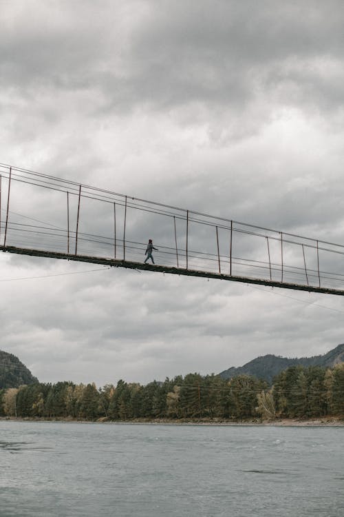 Free Person Crossing a Footbridge Over a River Stock Photo