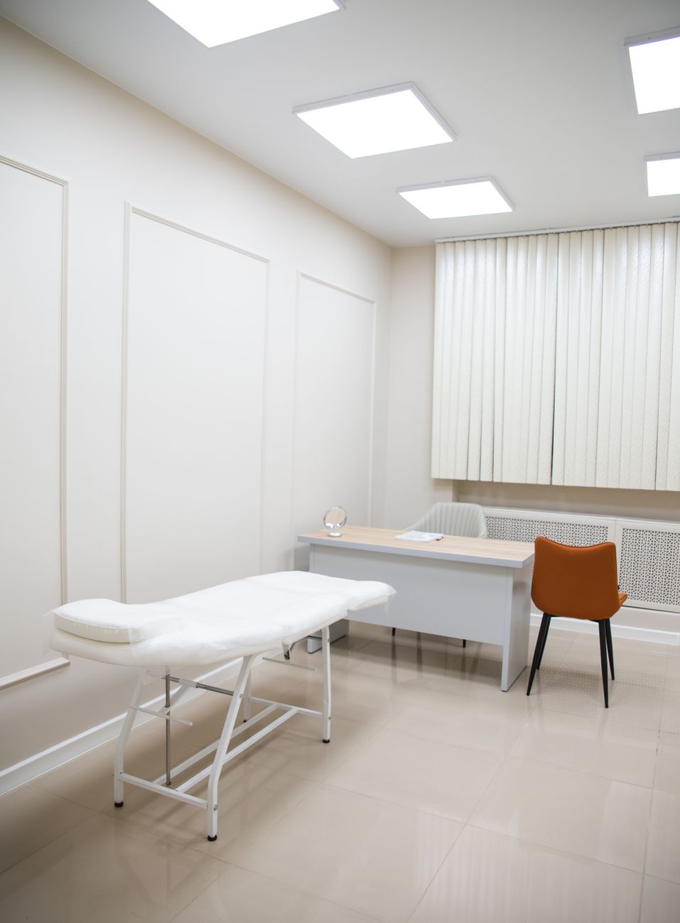 Bright white clinic room with exam table, desk, and chair, showcasing modern minimalist design.
