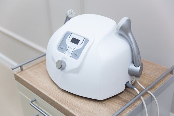 White professional facial machine on a shelf, its handpiece resting in the cradle