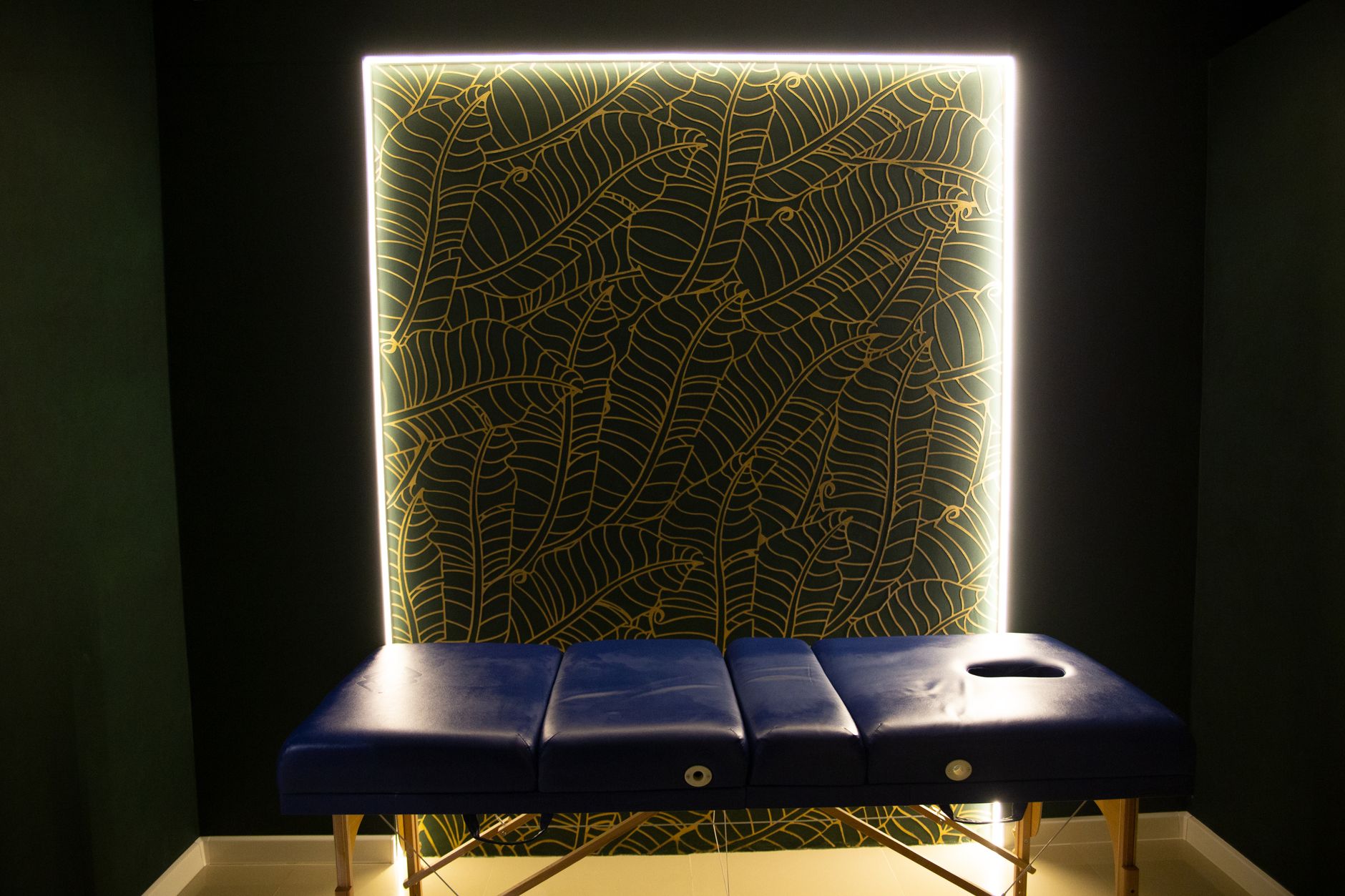 Elegant massage room featuring a blue massage table and stylish illuminated wall panel.