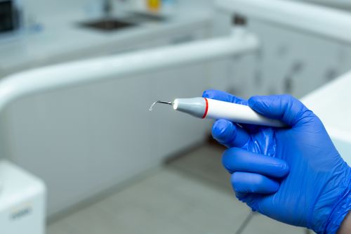 Free A dentist holds a dental scaler tool in a clinic, wearing blue gloves. Stock Photo