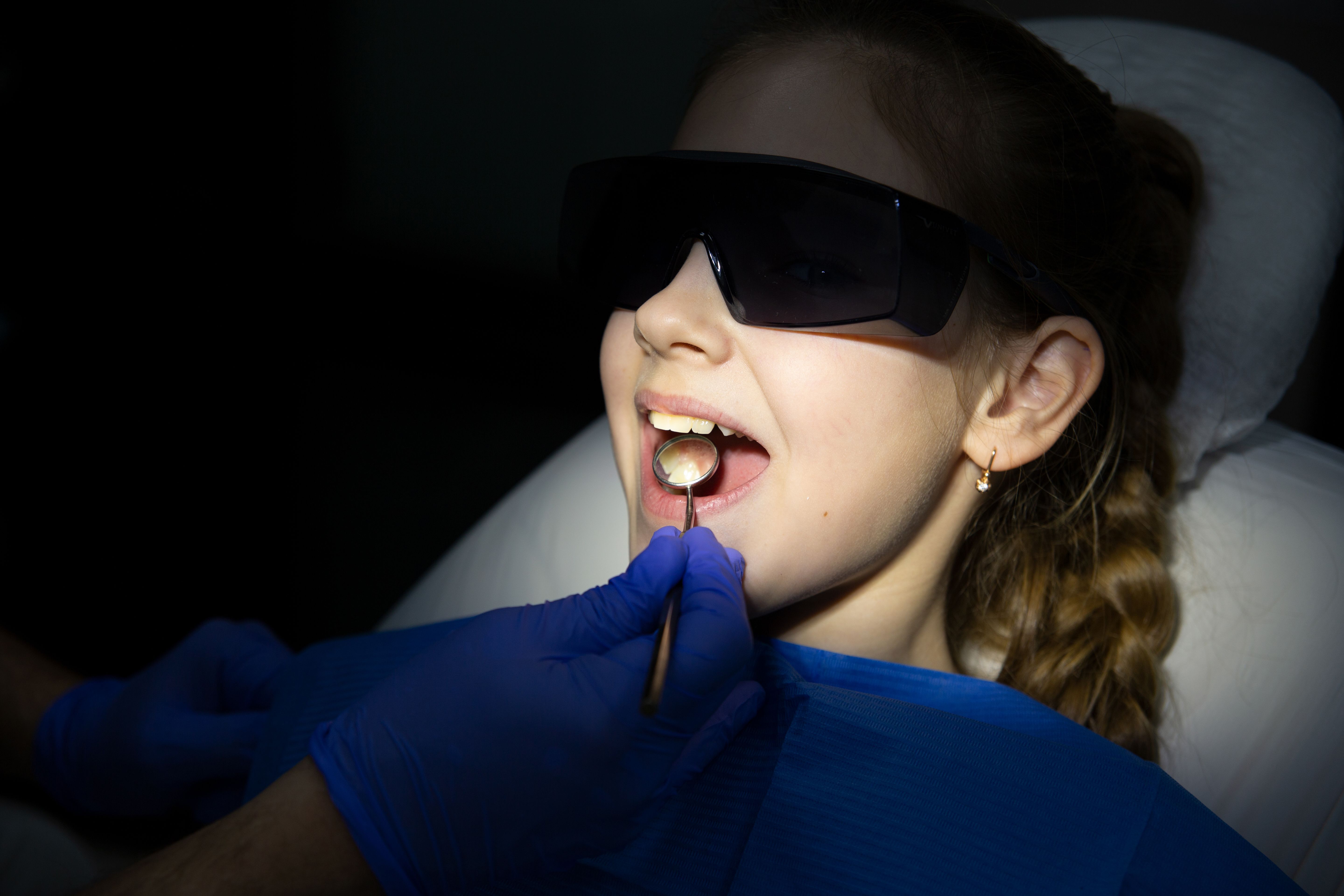Young girl having a dental examination using dental tools, wearing protective glasses at the dentist's office.