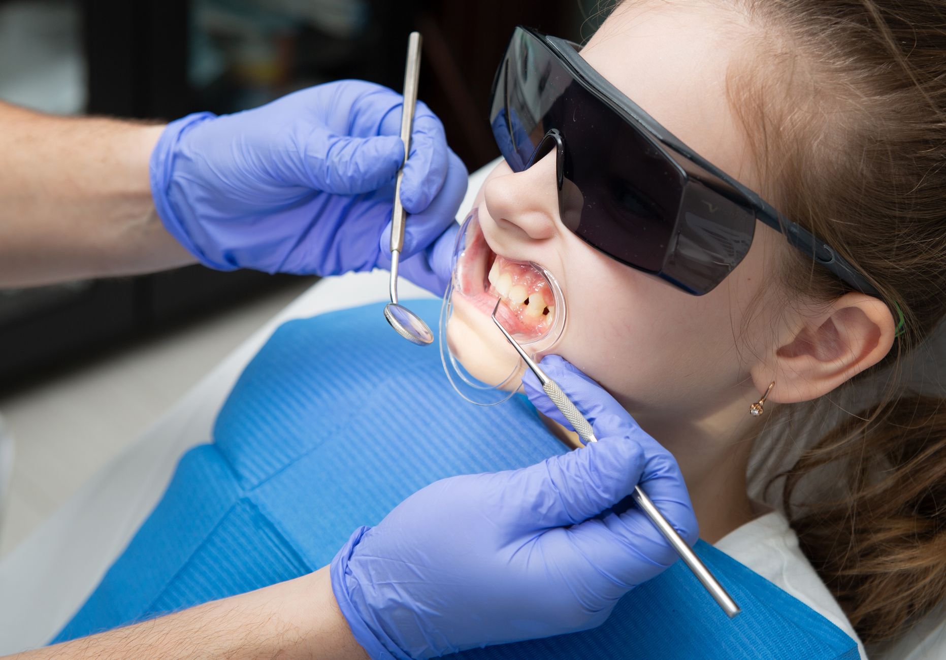 A young girl in protective glasses having her teeth checked by a dentist in a clinic