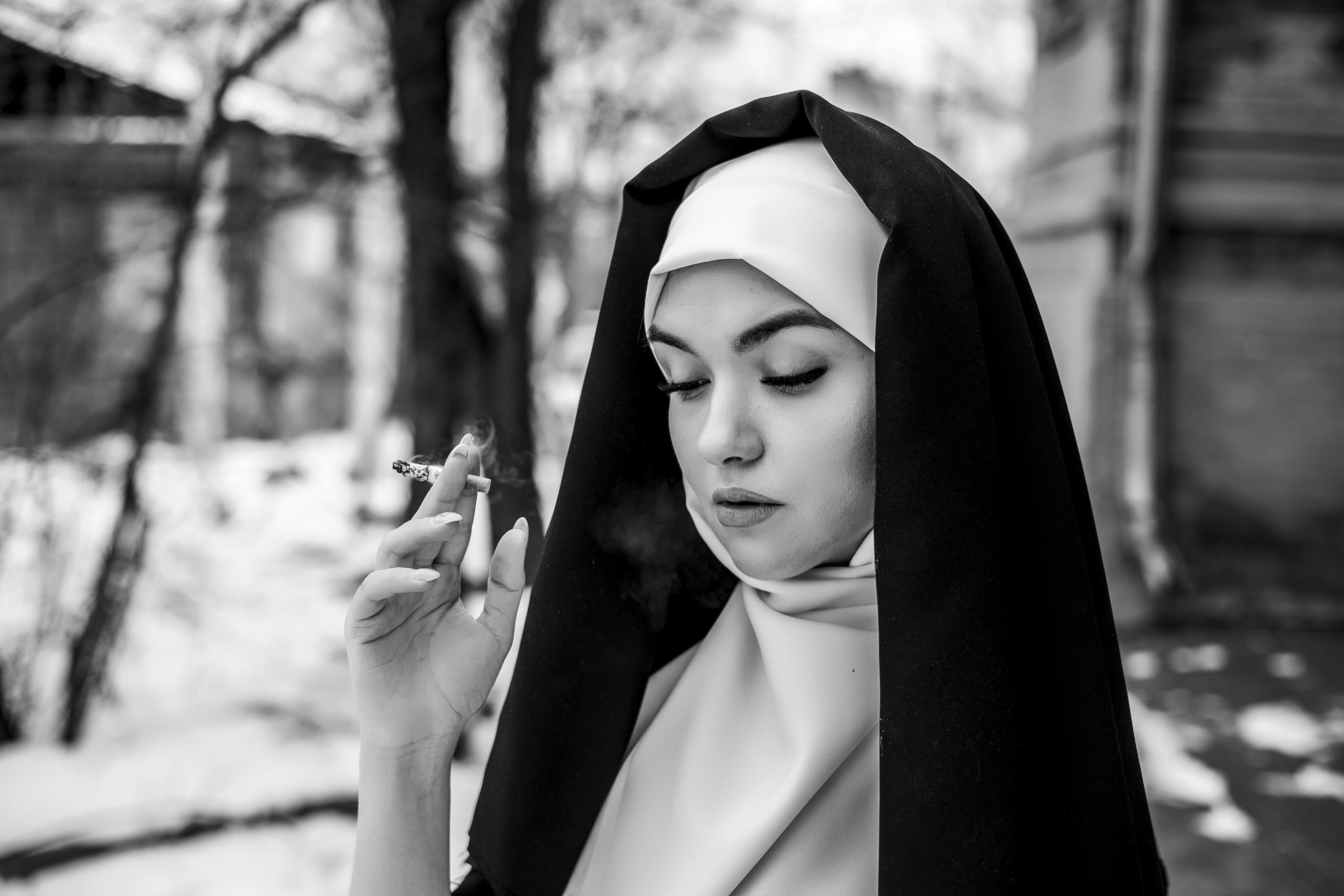 Thought-provoking black and white portrait of a nun smoking outdoors in winter.