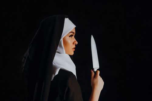 Free Side view of a nun holding a knife against a black background, creating a mysterious and intriguing scene. Stock Photo