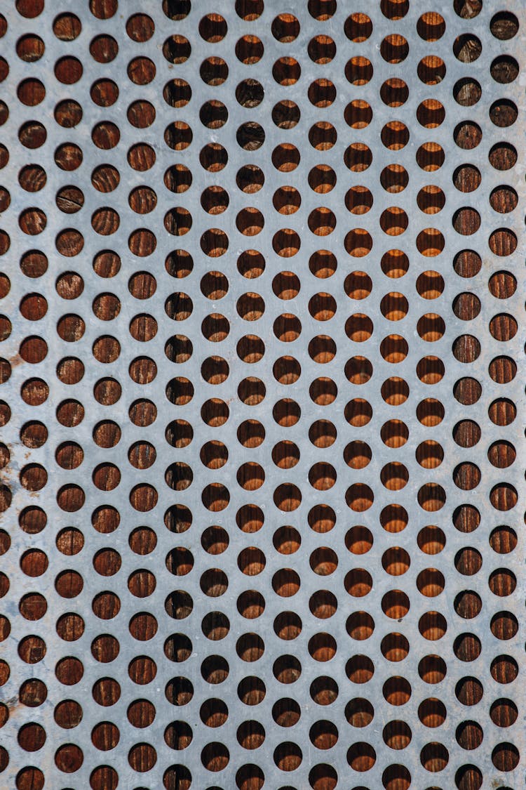 A Metal Sheet With Round Holes On A Wooden Surface