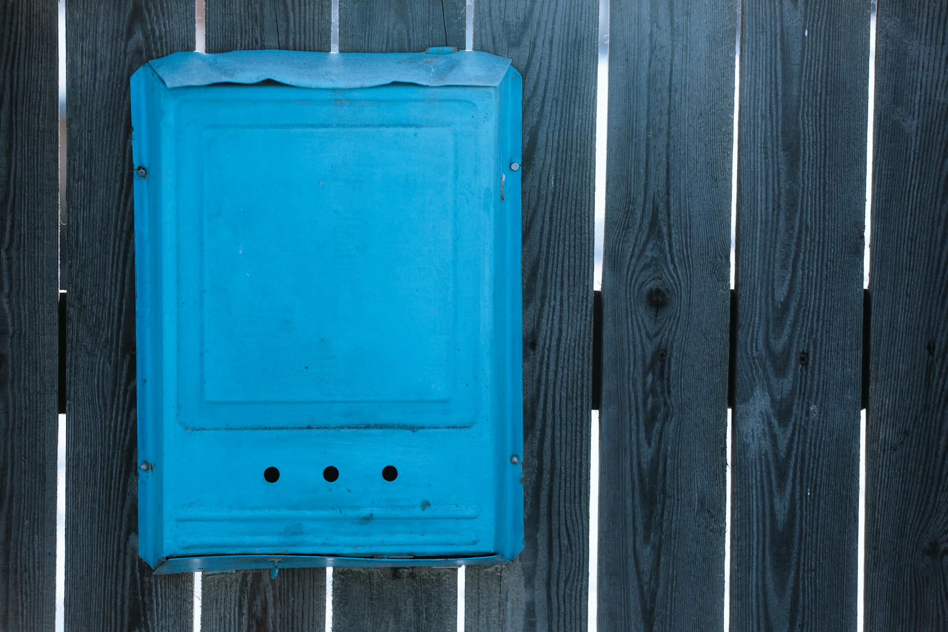A blue metal box with holes mounted on a rustic wooden fence outdoors.
