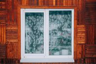 Close-up of a wooden house exterior with a floral curtain window revealing potted plants.