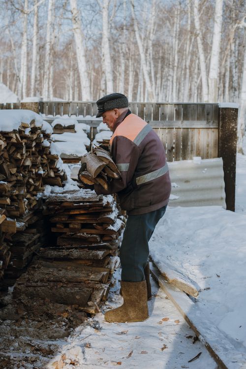 Free Senior man stacking firewood in a snowy landscape, showcasing winter chores. Stock Photo