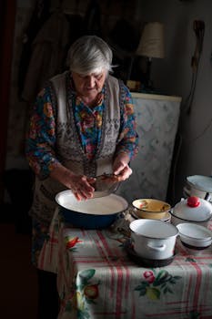 Elderly woman preparing food in a homely kitchen setting, showcasing traditional cooking style.