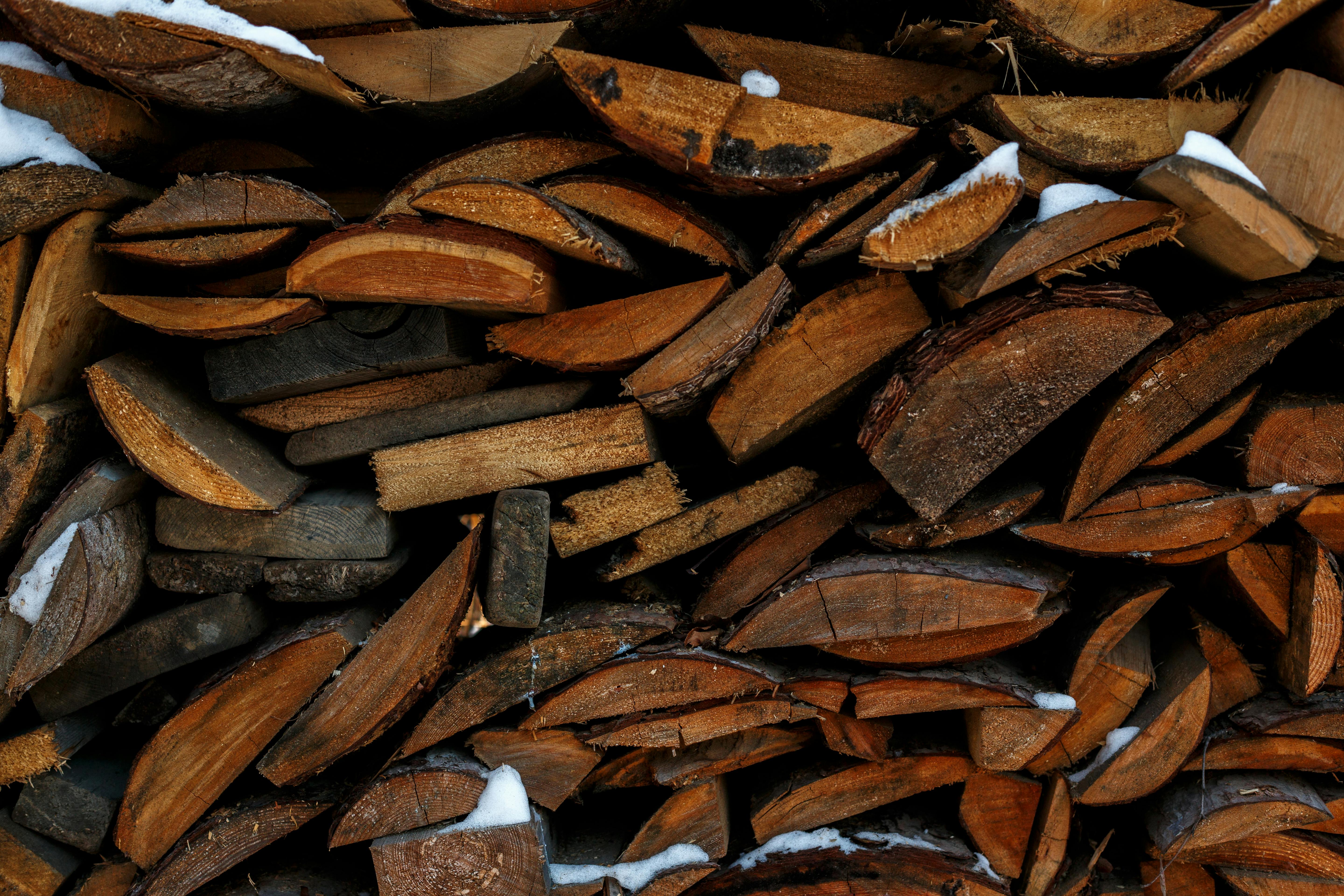 Close-up of stacked firewood with snow, showcasing natural textures and tones for rustic warmth.