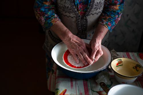 Free A senior woman washing a red dish in a vintage kitchen setting with floral patterns. Stock Photo