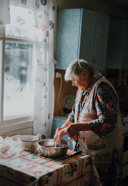 Free Senior woman preparing food in a sunlit kitchen, showcasing warmth and domestic life. Stock Photo