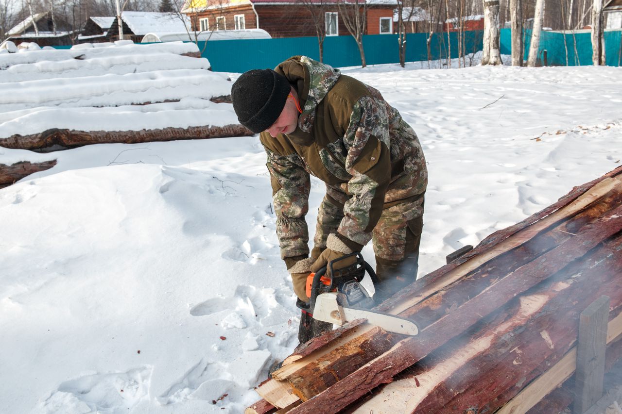 man in camouflage cuts wood with chainsaw in snowy winter setting