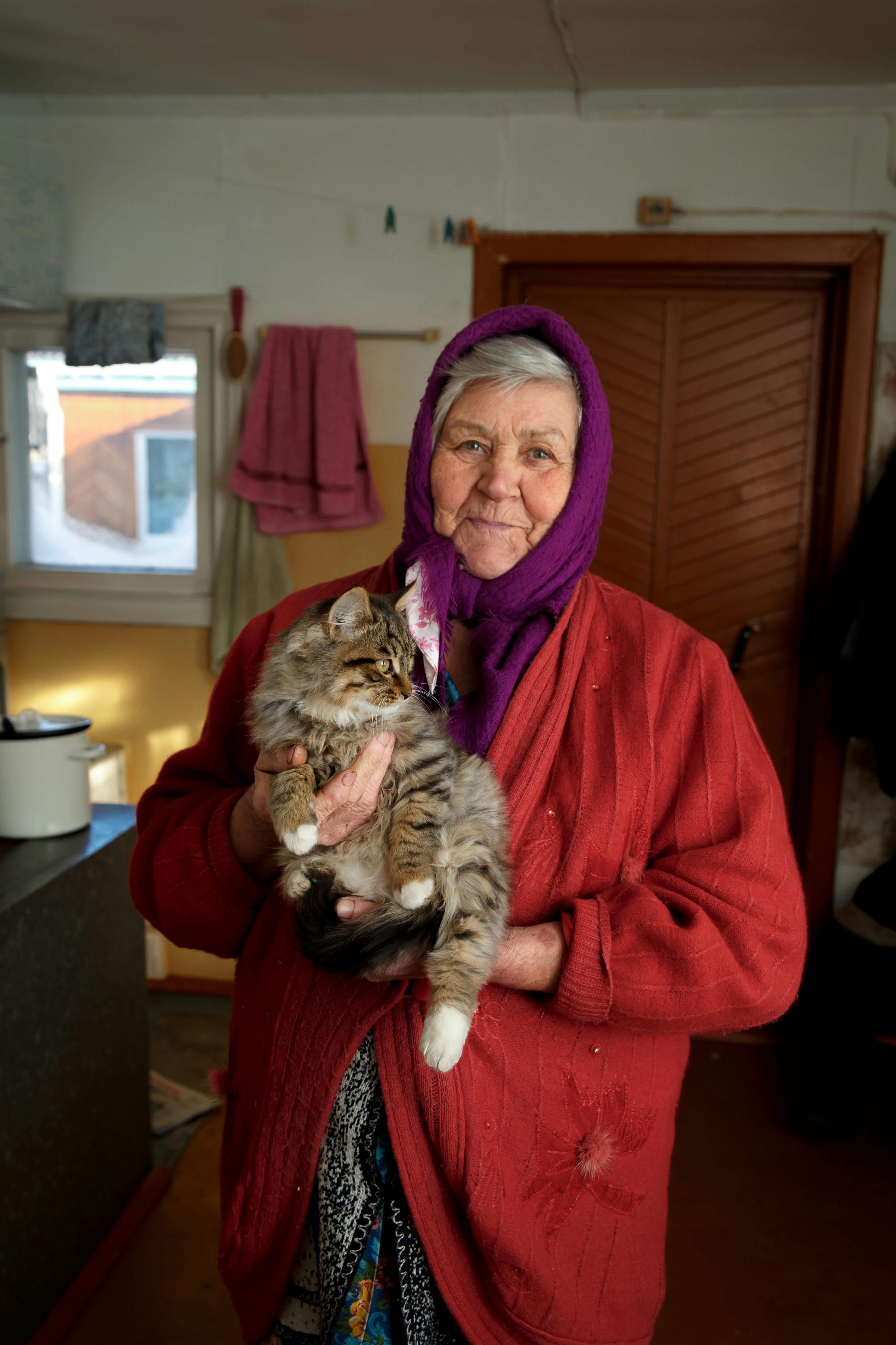 Senior woman in a headscarf holding a fluffy cat indoors, showcasing warmth and companionship.