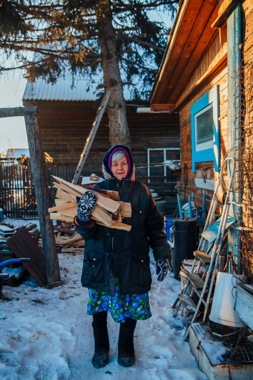 Free Senior woman in winter attire gathering firewood on a snowy day outdoors. Stock Photo