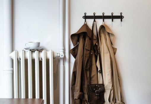 Coats and leather bag hanging against radiator with ceramic cup and saucer at home in daytime
